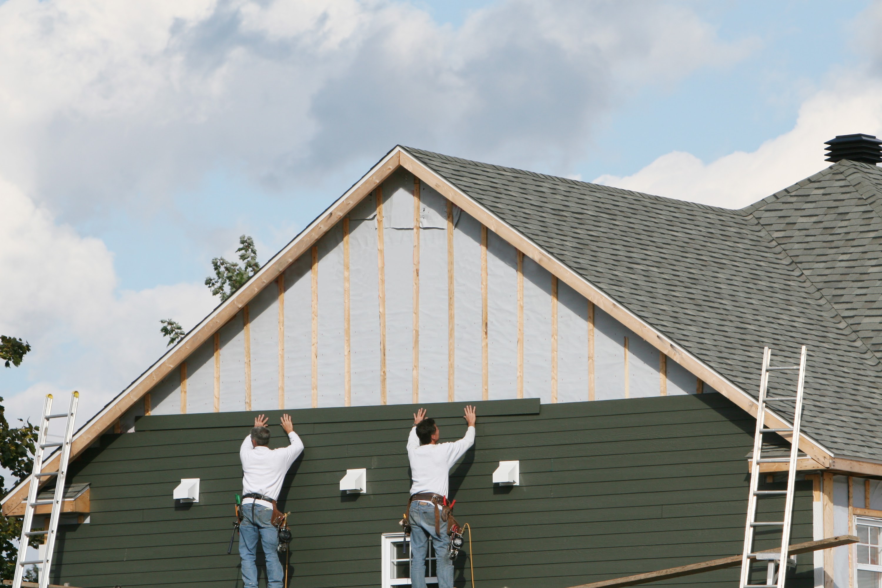 Two construction workers installing new aluminum siding on a house.